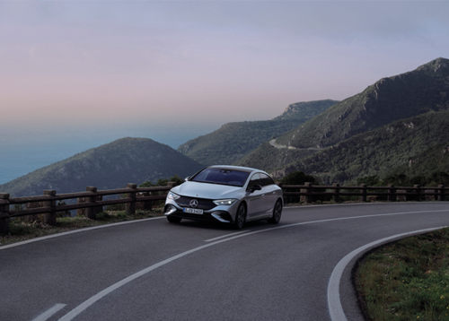 Ein Auto von Mercedes Benz fährt auf einer Straße in den Bergen. 