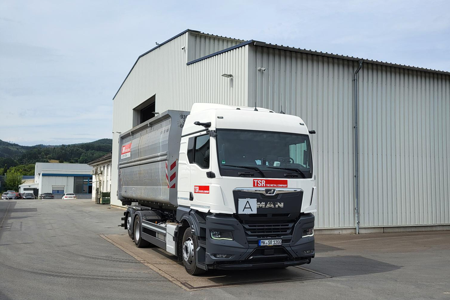 TSR LKW mit geladener Mulde steht vor einer Lagerhalle